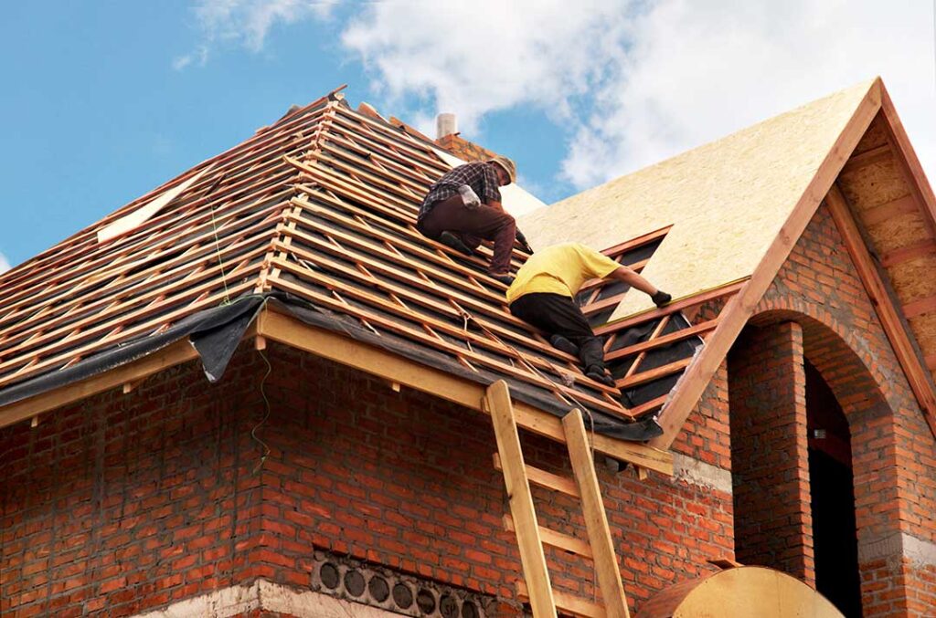 Roofing workers compare old shingles and exposed roof decking on a residential house.