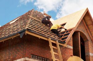 Roofing workers compare old shingles and exposed roof decking on a residential house.